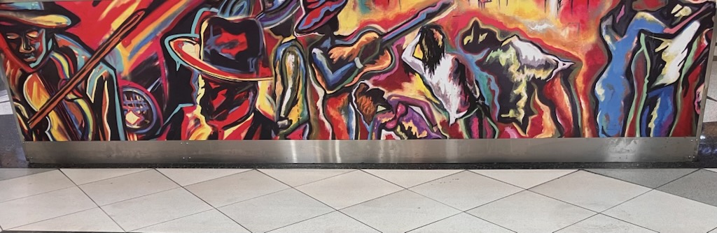 Detail of an airport concourse mural showing musicians and dancers in red, gold, and blue by Corey Barksdale