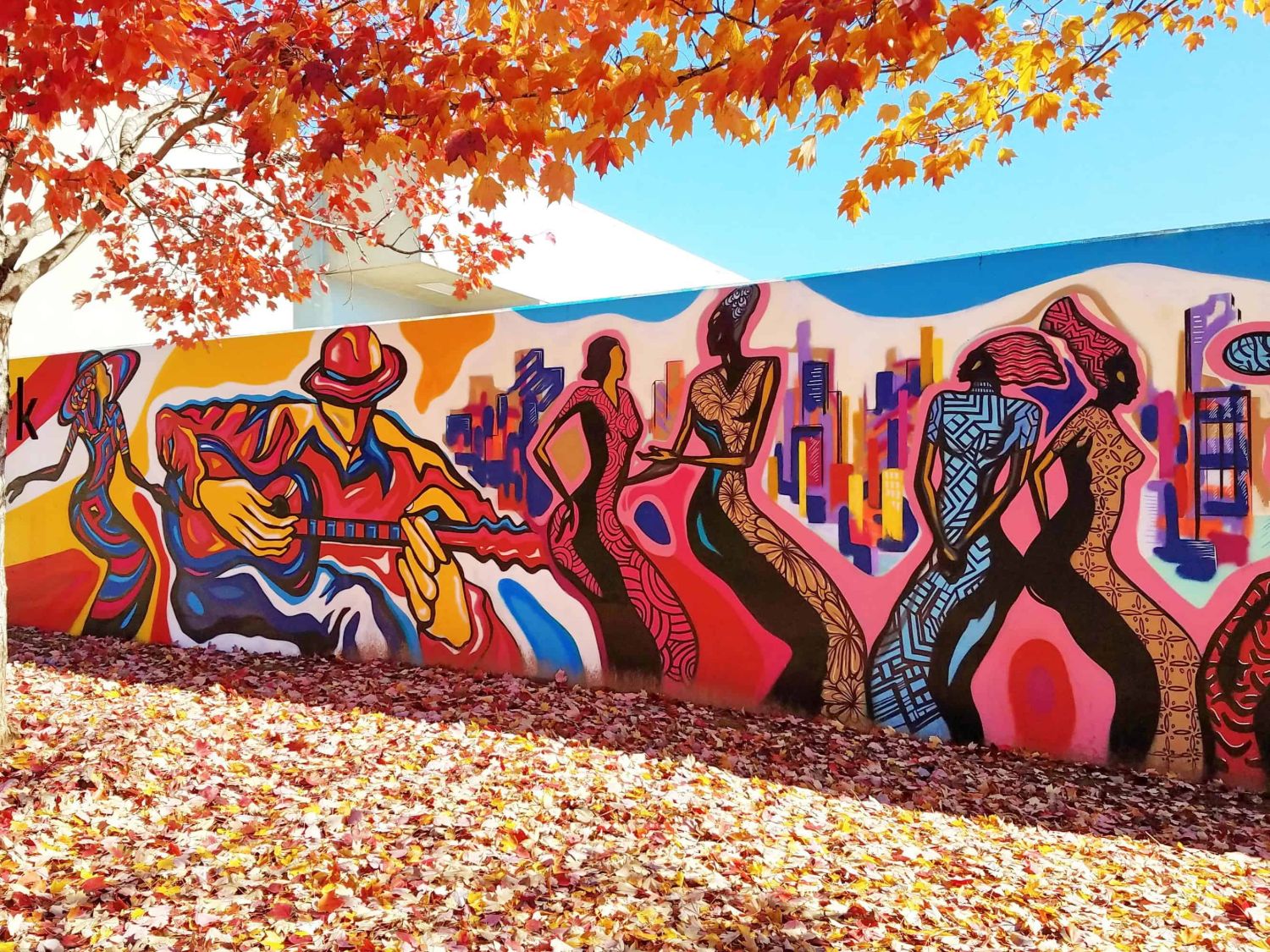 Outdoor mural of a guitarist and dancing figures with a city skyline, painted by muralist Corey Barksdale