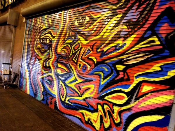 Roll-down security gate painted with a fiery abstract face mural, photographed at night