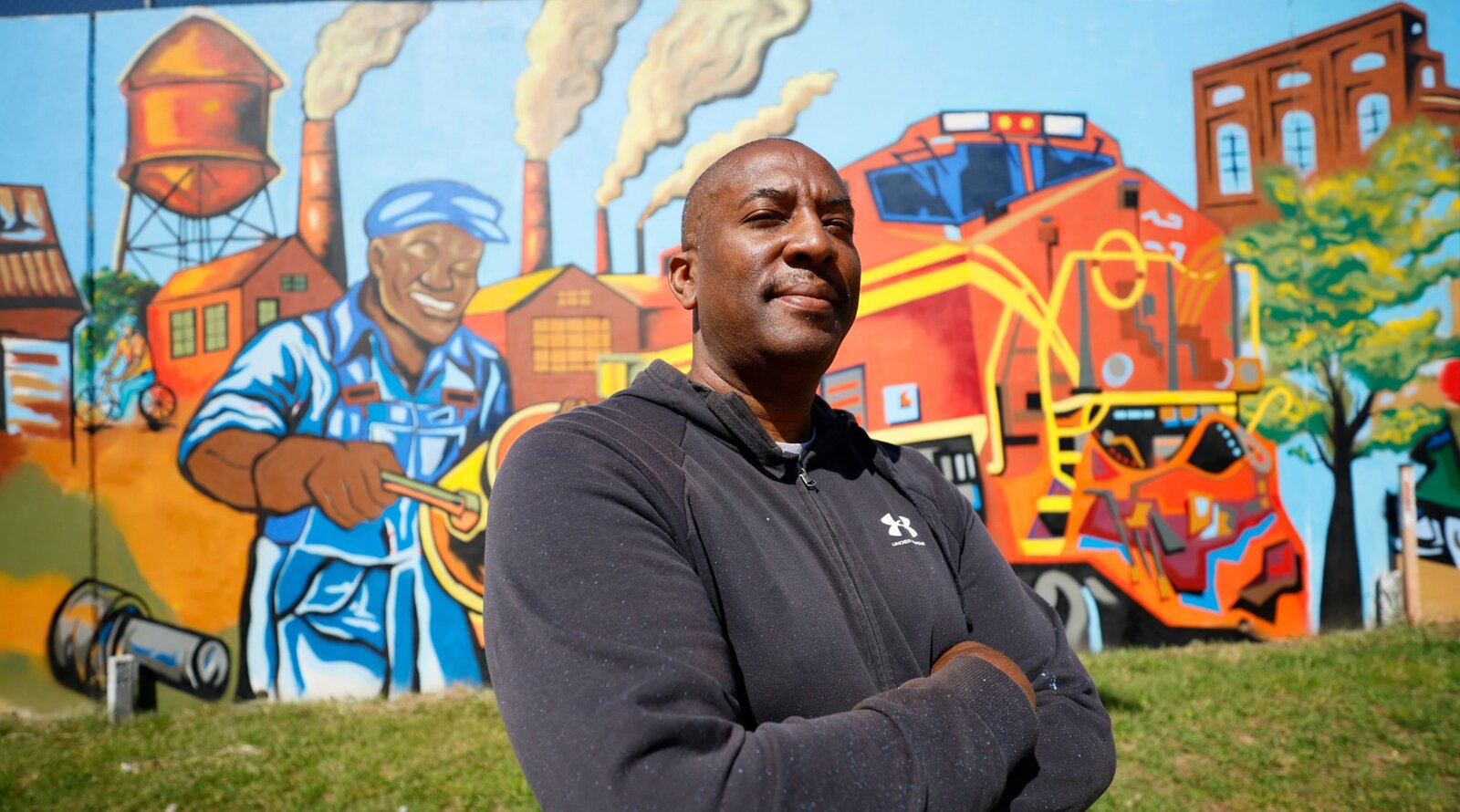 Portrait of Atlanta muralist Corey Barksdale standing in front of the completed industrial heritage panel of the Blandtown mural