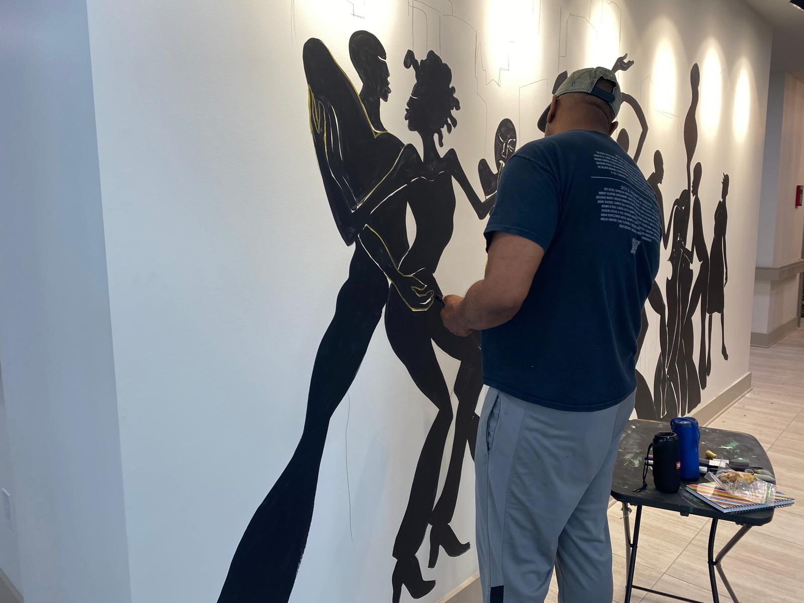 Corey Barksdale detailing a black silhouette dancing couple with gold linework for the Decatur East mural at The Link at Columbia