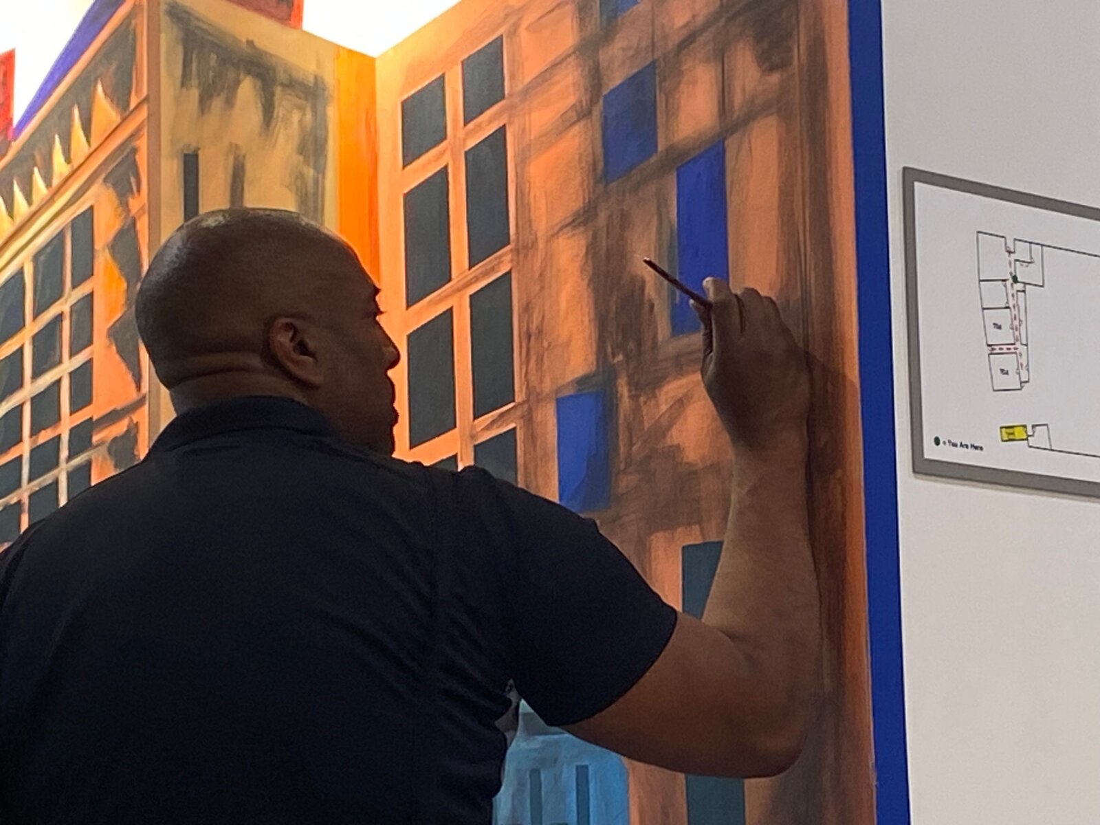 Corey Barksdale painting architectural building detail on the Decatur East mural beside a hallway wayfinding map