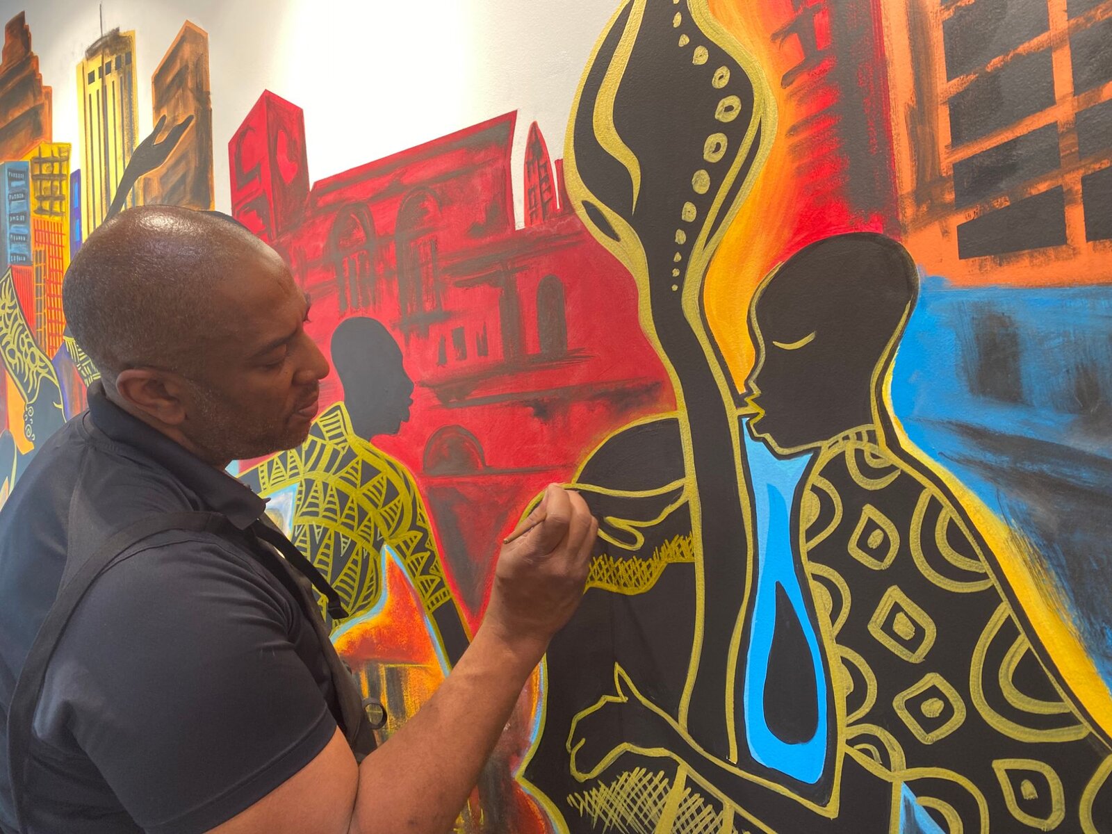 Close-up of Corey Barksdale painting African-pattern textile detail on a silhouetted figure in the Decatur East mural