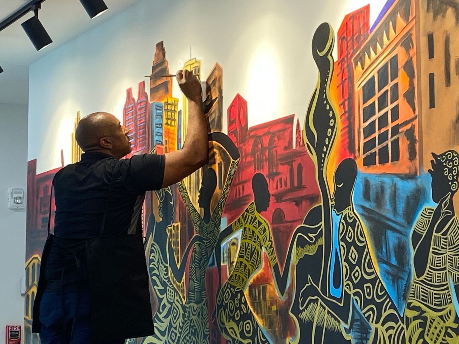 Corey Barksdale painting the Atlanta skyline backdrop of the Decatur East mural, reaching up to detail the building tops