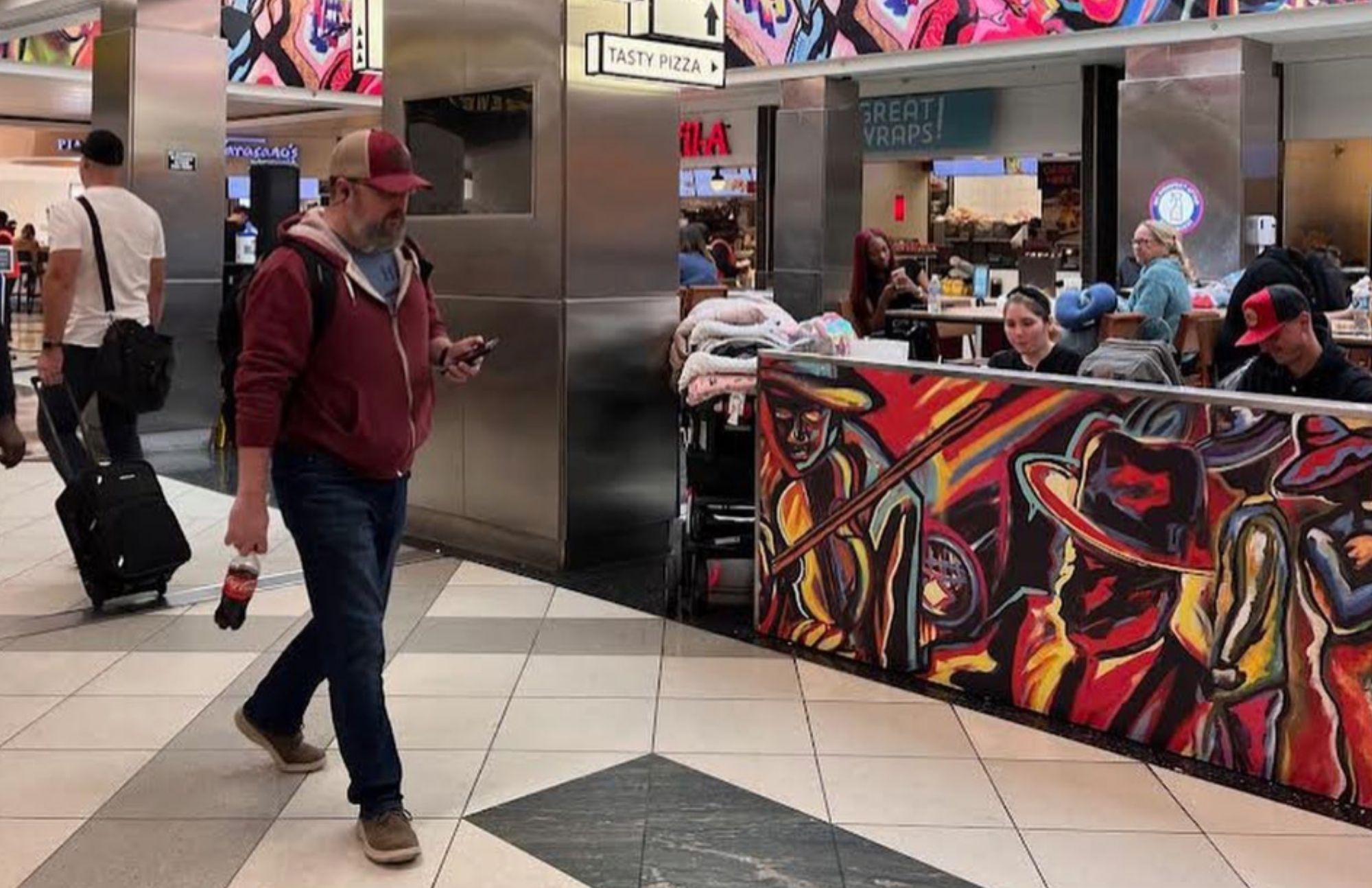 A traveler walks past Corey Barksdale's mural on the Concourse A food court partition wall at Hartsfield-Jackson Atlanta International Airport
