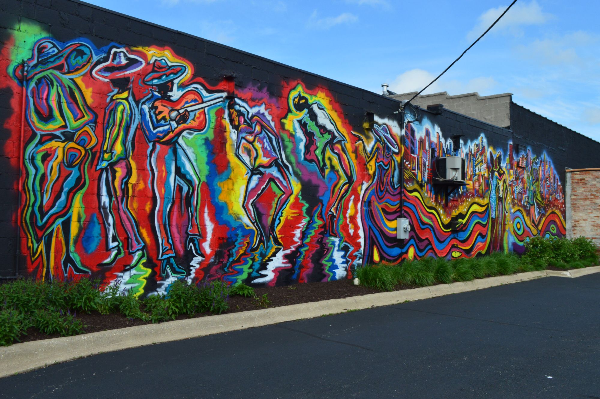 Wide daylight view of Corey Barksdale's CRE8IV mural in downtown Rockford, Illinois, showing musicians and dancers in vivid color on a black wall