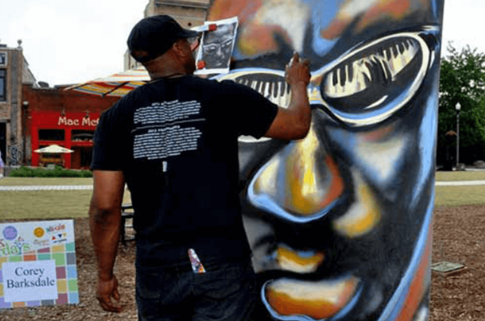 Corey Barksdale live painting a jazz musician mural on a community column at an outdoor Atlanta event